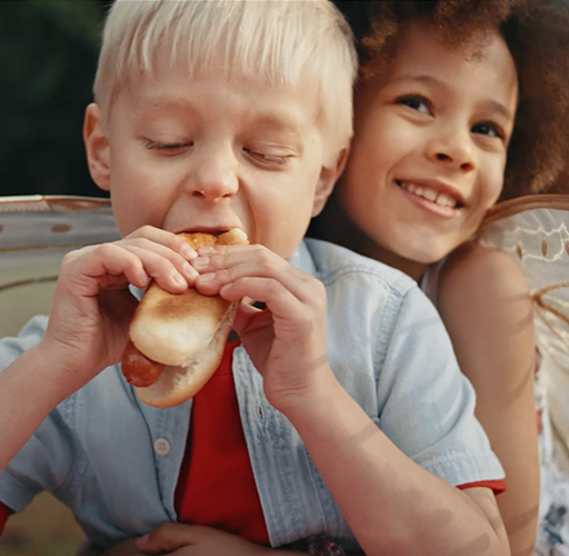 Children hugging while one is eating a hotdog in a Dempster's bun
